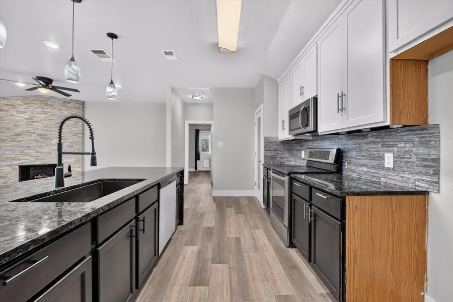 Kitchen sink run under pendant lights looking down the first floor hall at 716 River Hill Ln