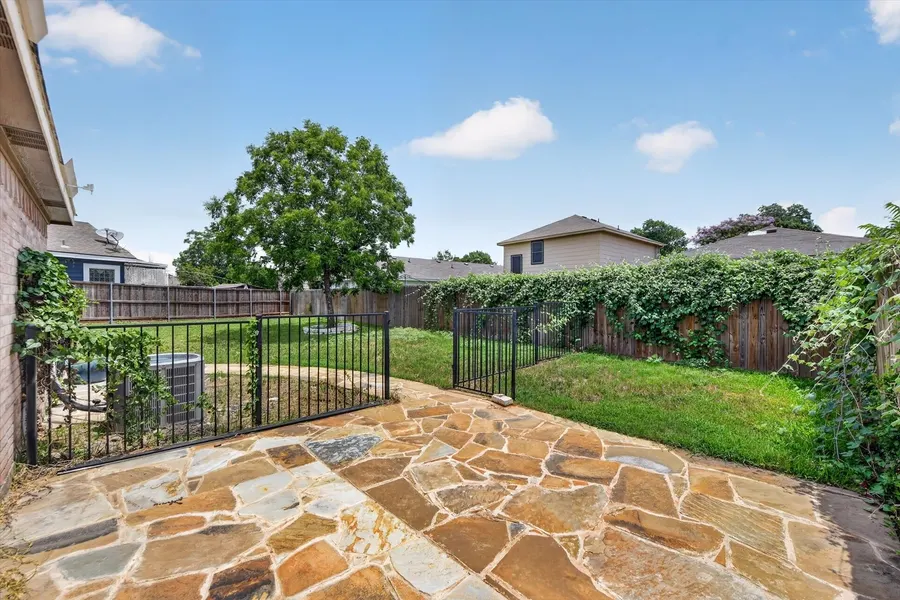 Flagstone patio framed by a wrought iron fence and mature shade trees at 716 River Hill Ln